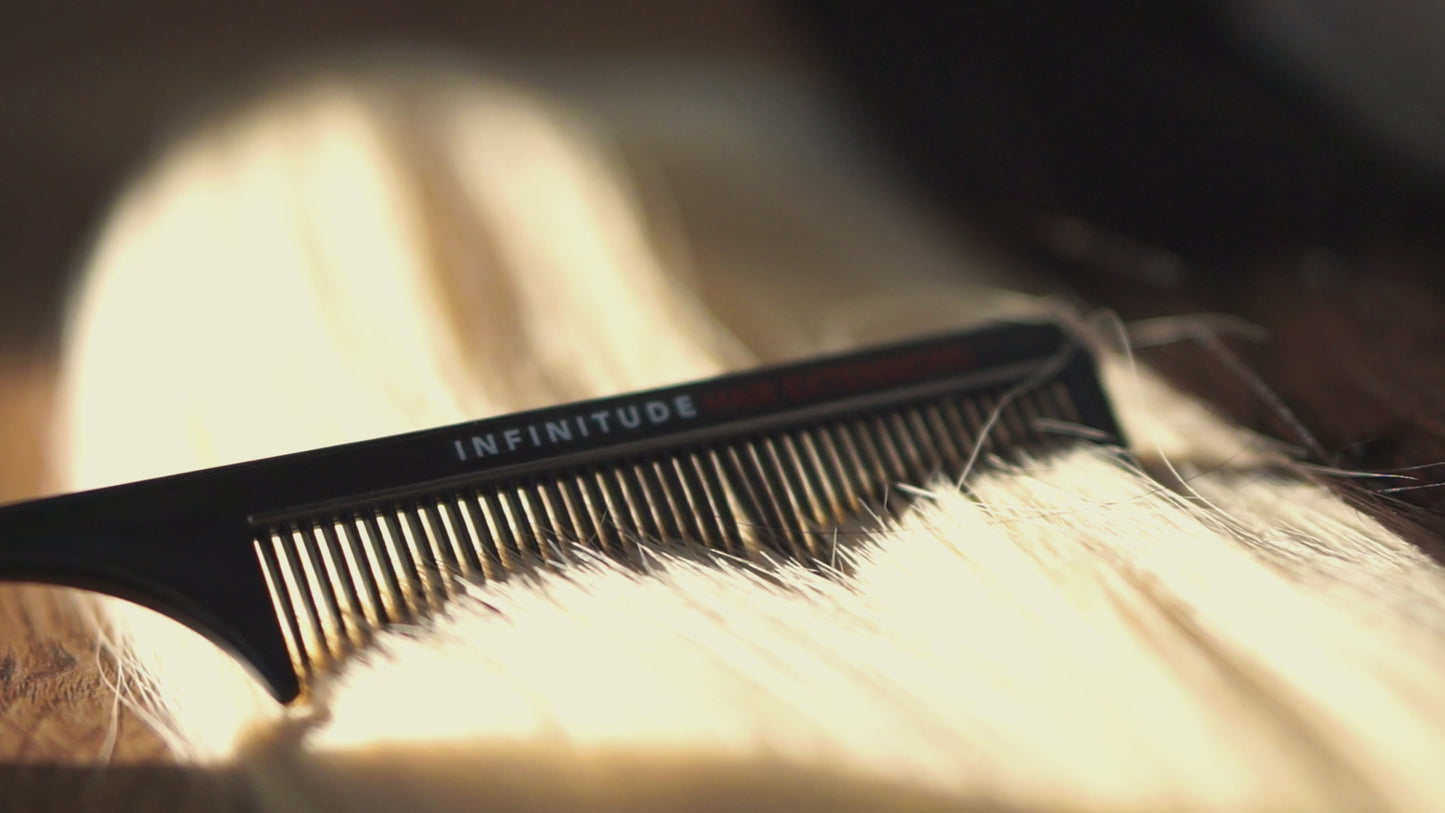 A black Infinitude Hair Extensions comb is slowly combing through blonde extensions in natural sunlight